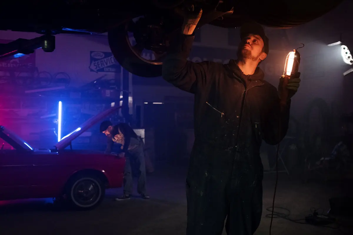 Mechanic inspecting the underside of a vehicle in a neon-lit workshop